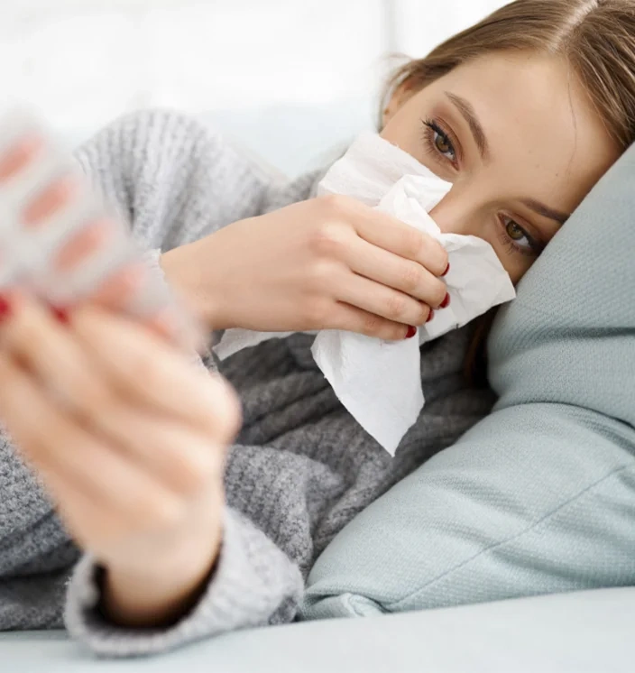 девушка с простудой держит антибиотик в руке